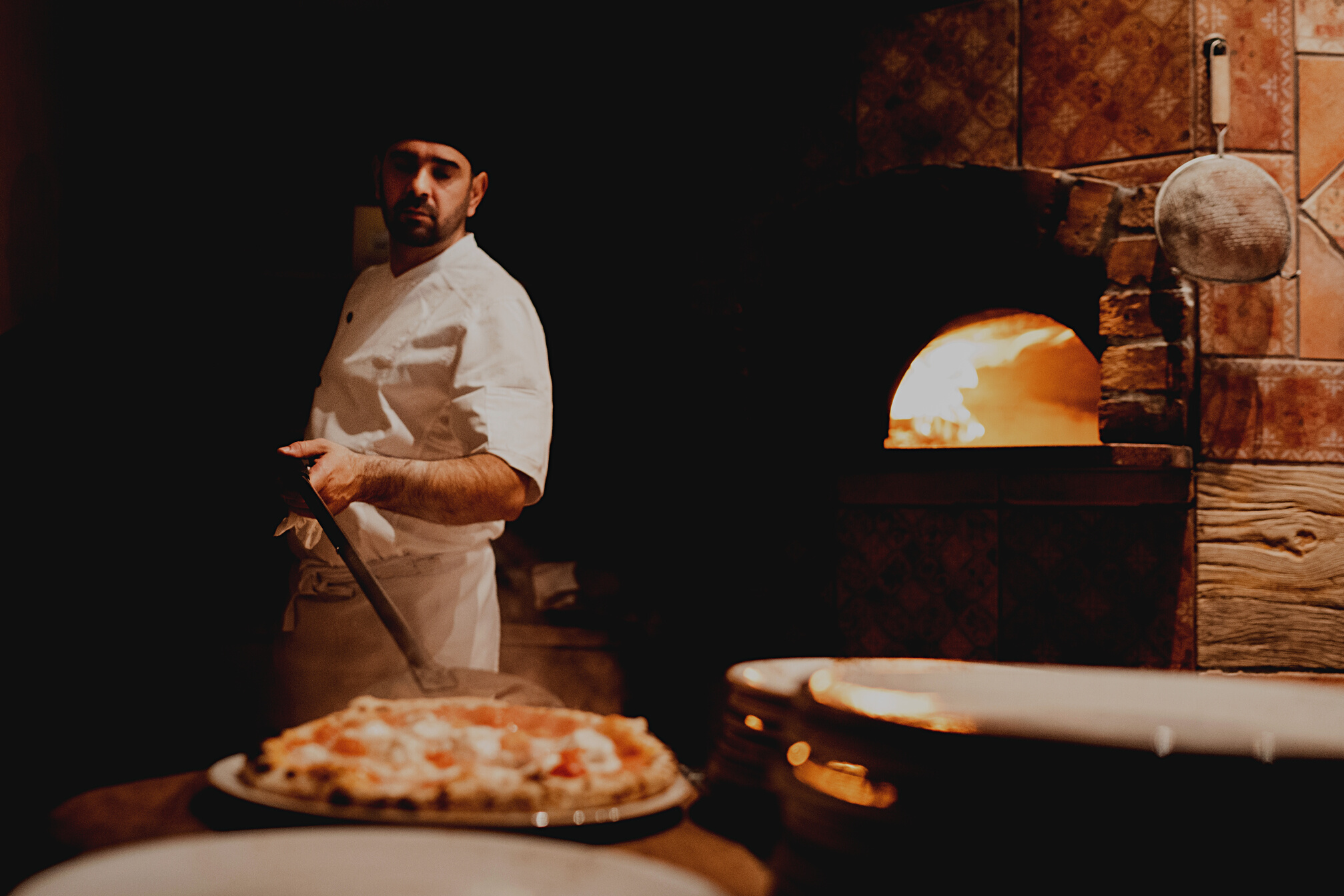 Pizza maker plating a freshly baked Neapolitan pizza with a peel